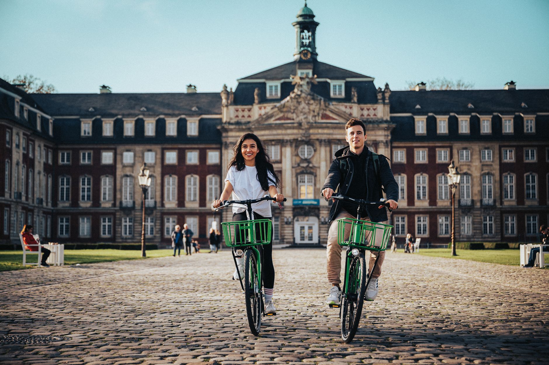 Two students cycling across a European university square